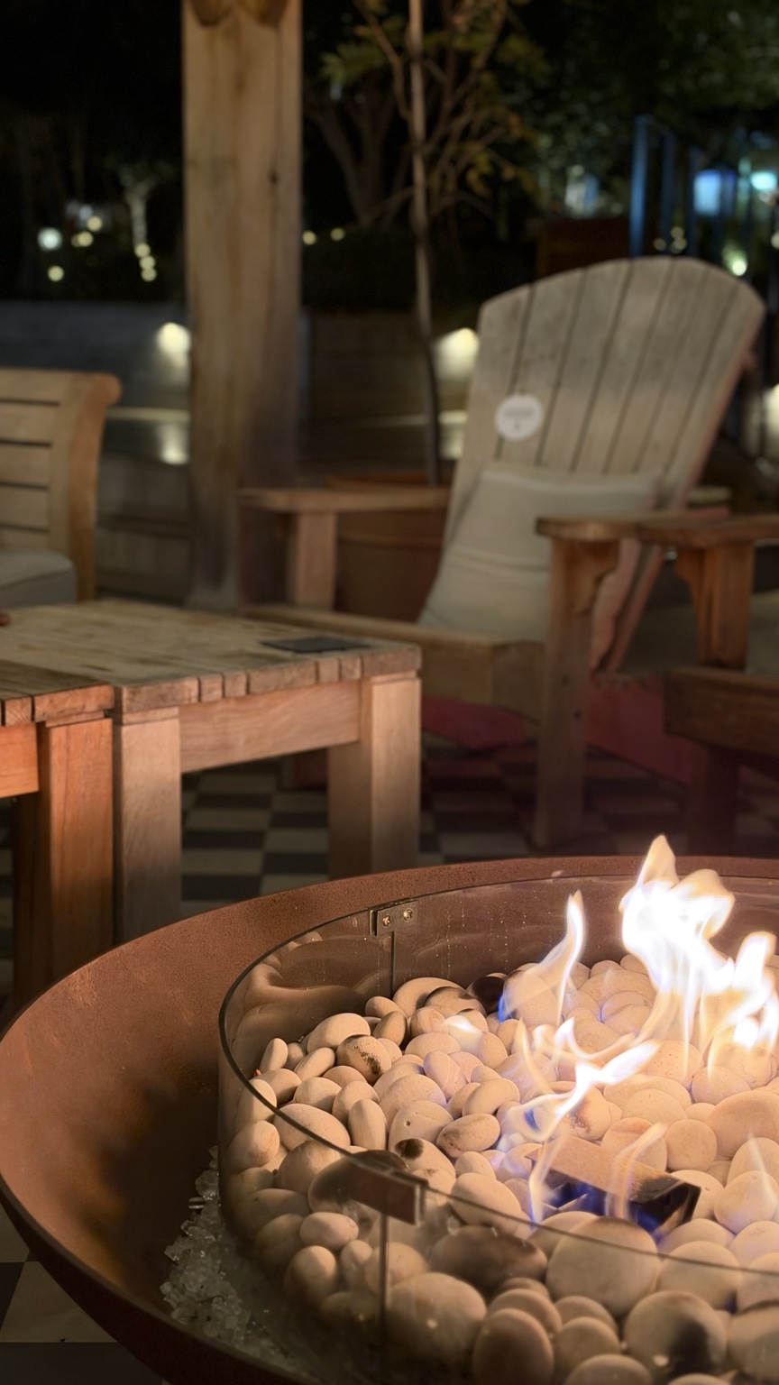 Fire pit glowing among outdoor lounge chairs at Eden Hall after dark